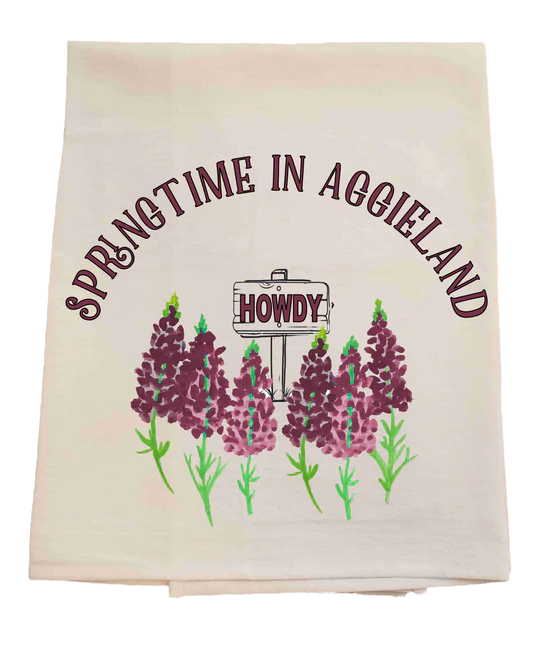 Tea towel with 'Springtime in Aggieland' and 'Howdy' text, featuring purple flowers on a pastel background.
