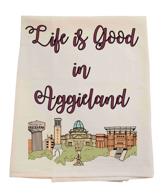 Tea towel with 'Life is Good in Aggieland' text and university buildings illustration.