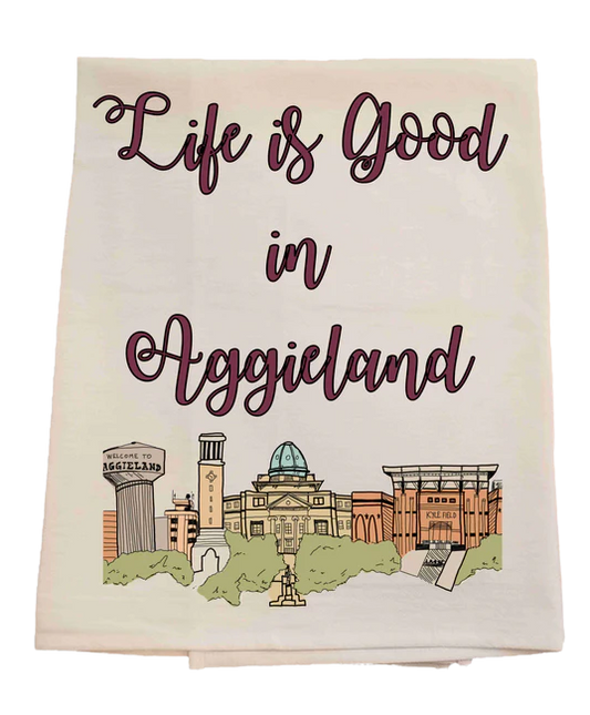 Tea towel with 'Life is Good in Aggieland' text and university buildings illustration.