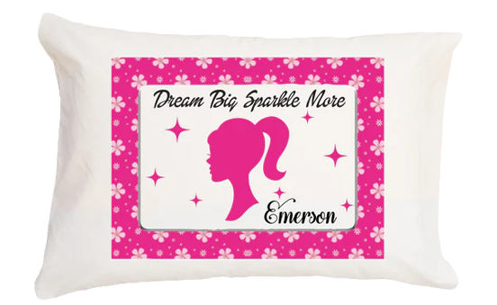Decorative pillow with pink silhouette of a girl, text 'Dream Big Sparkle More' and name 'Emerson' on a white background.