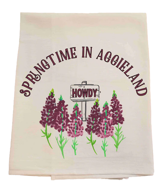 Tea towel with 'Springtime in Aggieland' and 'Howdy' text, featuring purple flowers on a pastel background.